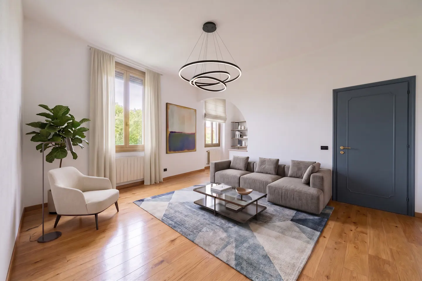 Bright living room with wood floors, a gray sectional sofa, a geometric rug, and a modern ring chandelier.