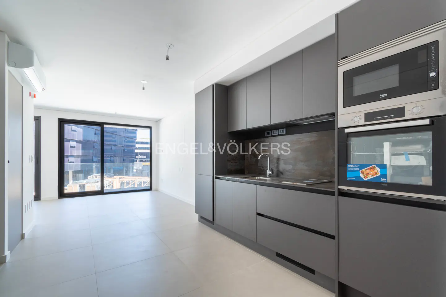 A modern apartment interior with gray cabinets, stainless steel appliances, and a large sliding glass door leading to a balcony.