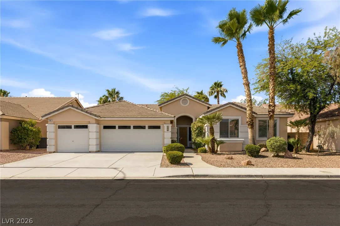 Single-story beige stucco home with a three-car garage, desert landscaping, and tall palm trees under a blue sky.