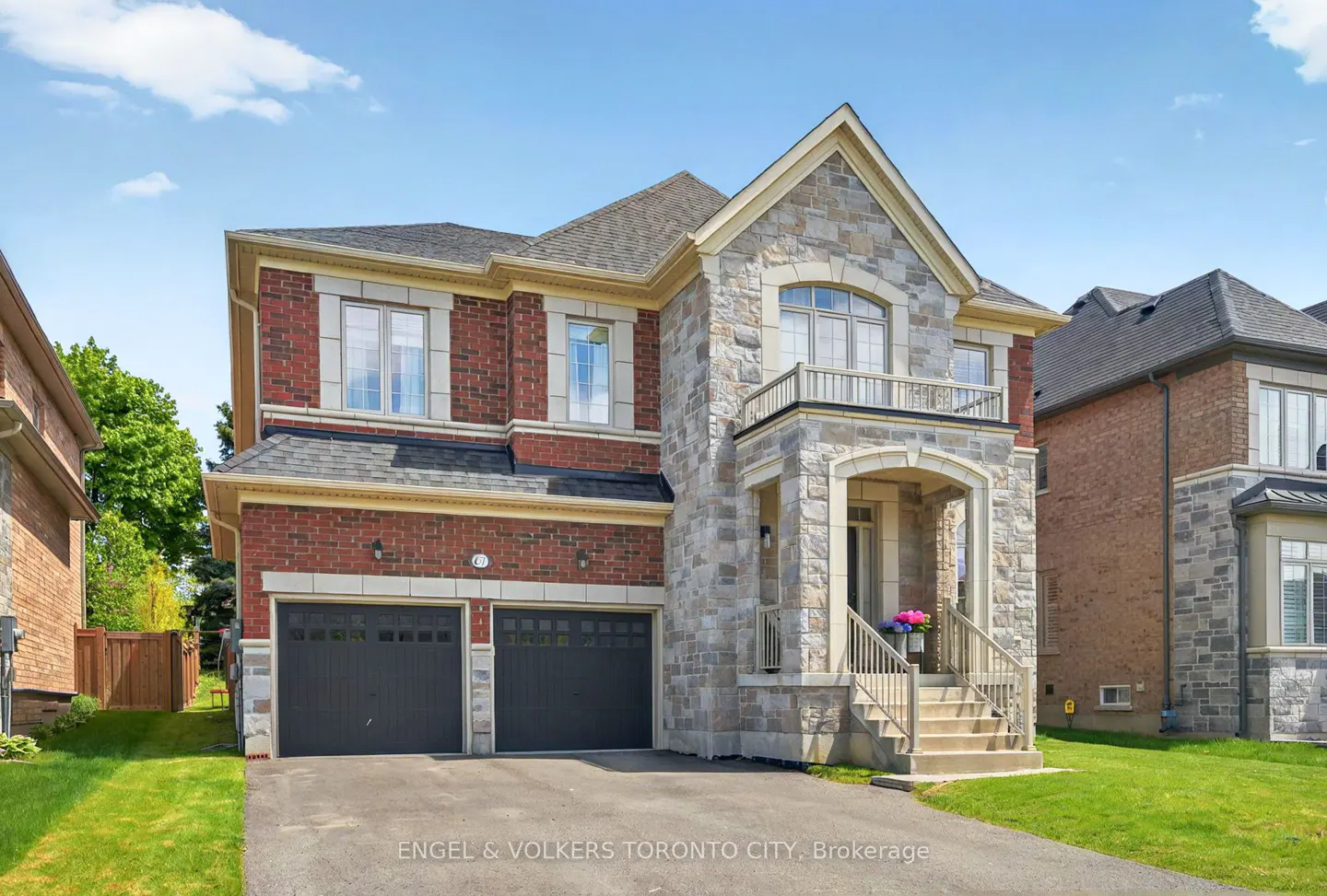 Two-story house with brick and stone facade, black garage doors, and a small balcony under a blue sky.