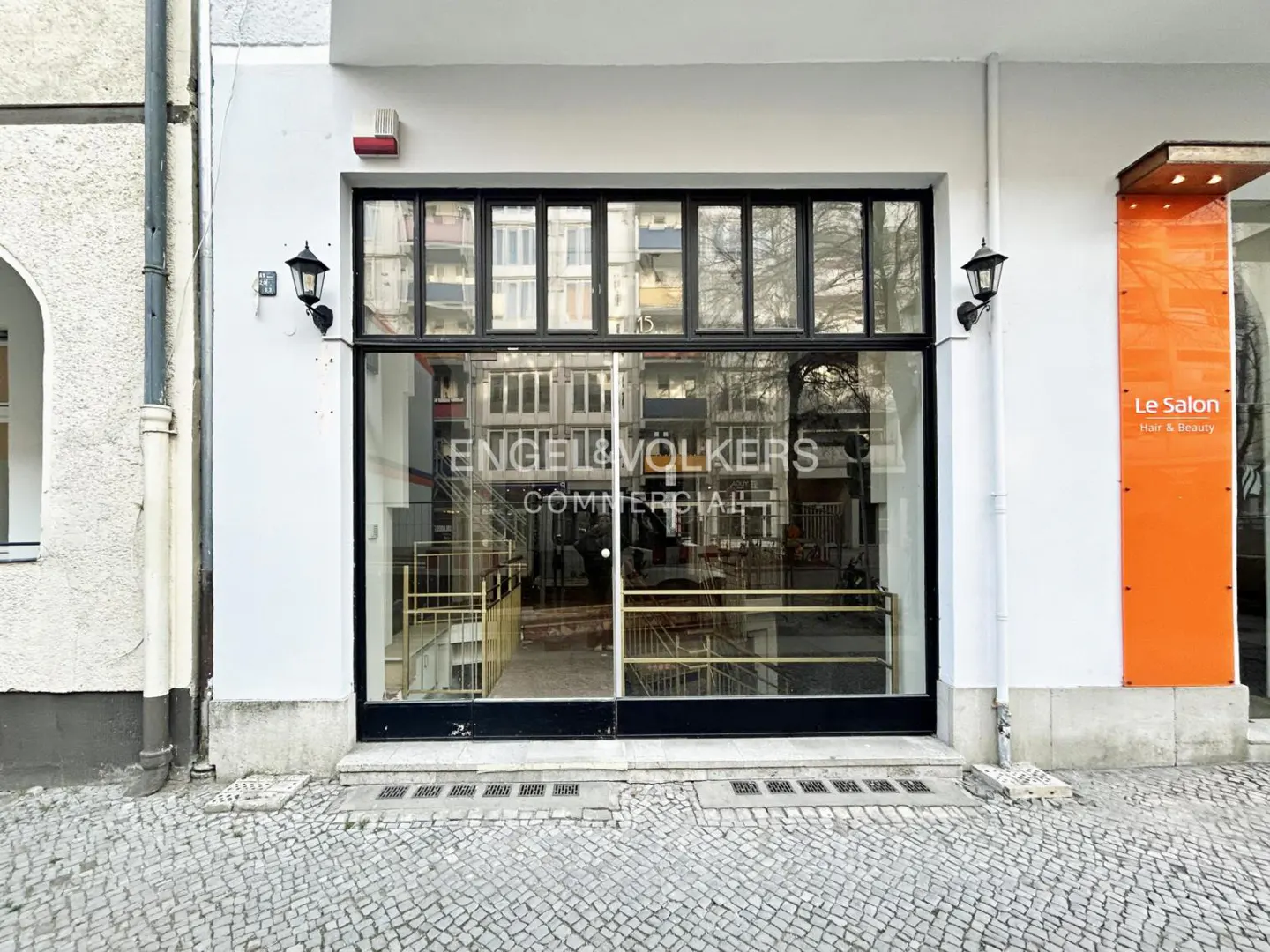 Exterior view of Engel & Volkers Commercial office with a large glass window and black frame. Cobblestone street in front.