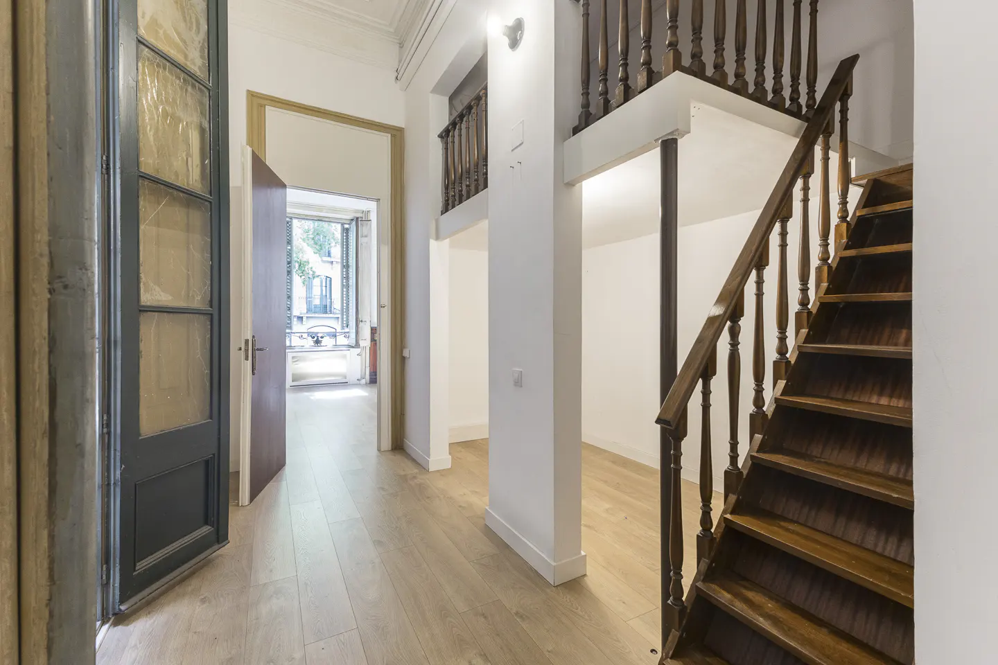 Interior view of a home featuring a wooden staircase, light wood floors, and an open doorway leading to a balcony.