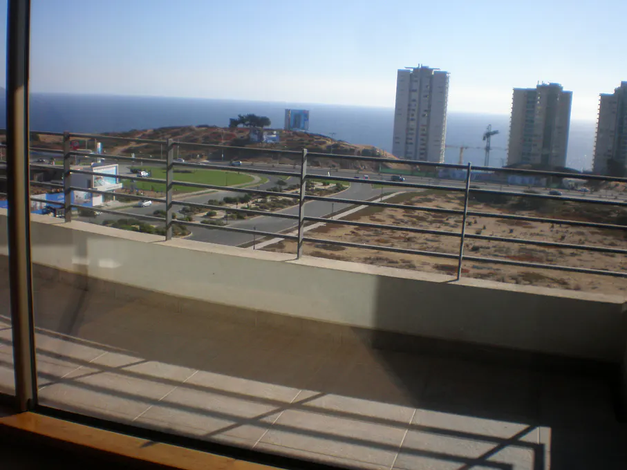 View from a balcony with a metal railing overlooking a coastal city with tall buildings and the ocean.