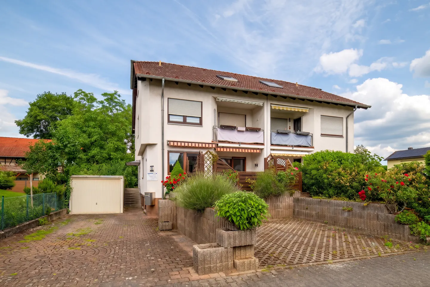 Two-story white residential building with a tiled roof, balconies, a paved driveway, and a detached garage.