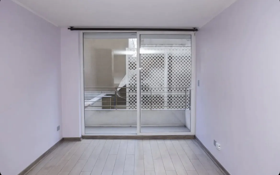 Empty room with light purple walls, light wood floors, and sliding glass doors to a balcony with a white lattice screen.