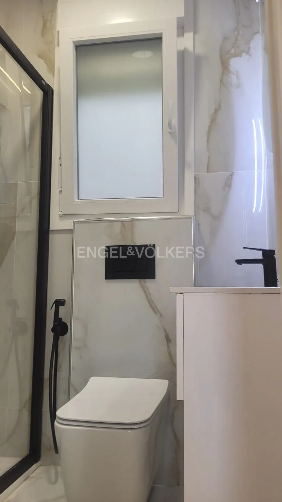 Modern bathroom with white toilet, marble walls, and black fixtures. Engel & Volkers logo is visible.