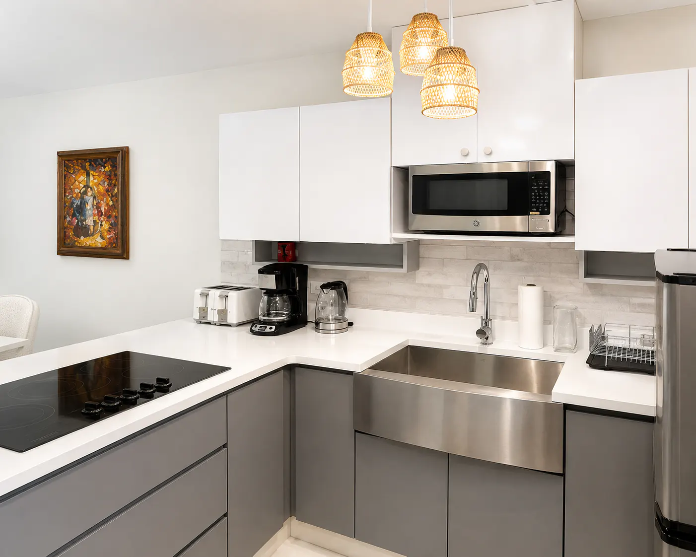 Modern kitchen with white cabinets, gray lower cabinets, stainless steel sink, and woven pendant lights.