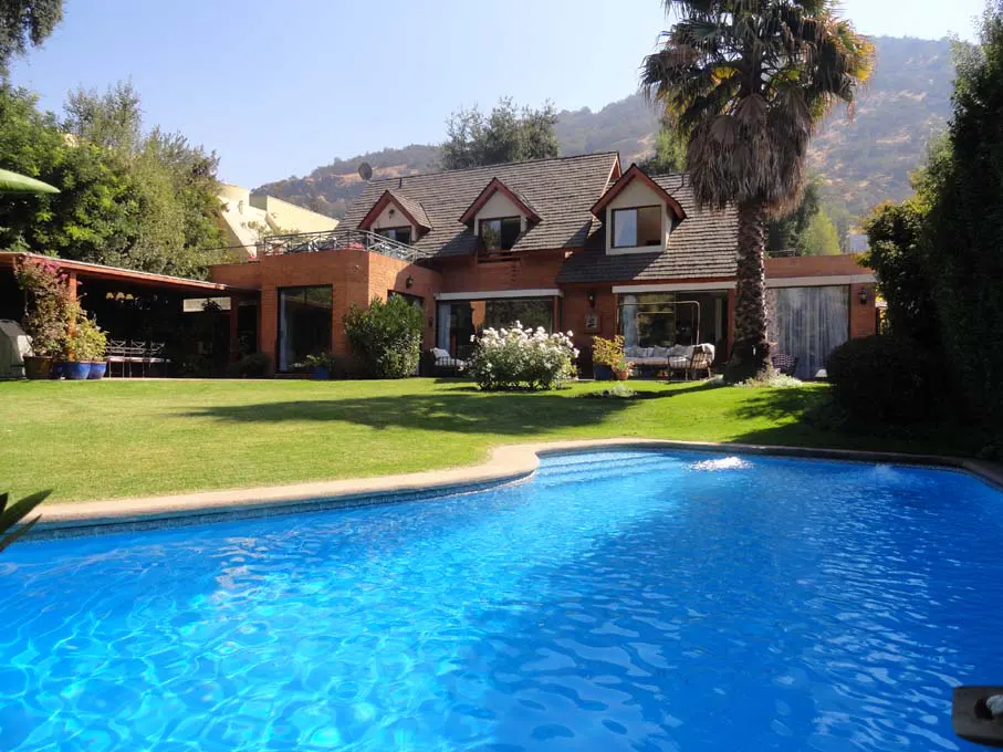 A brick house with a pool and green lawn on a sunny day. Mountains are in the background.