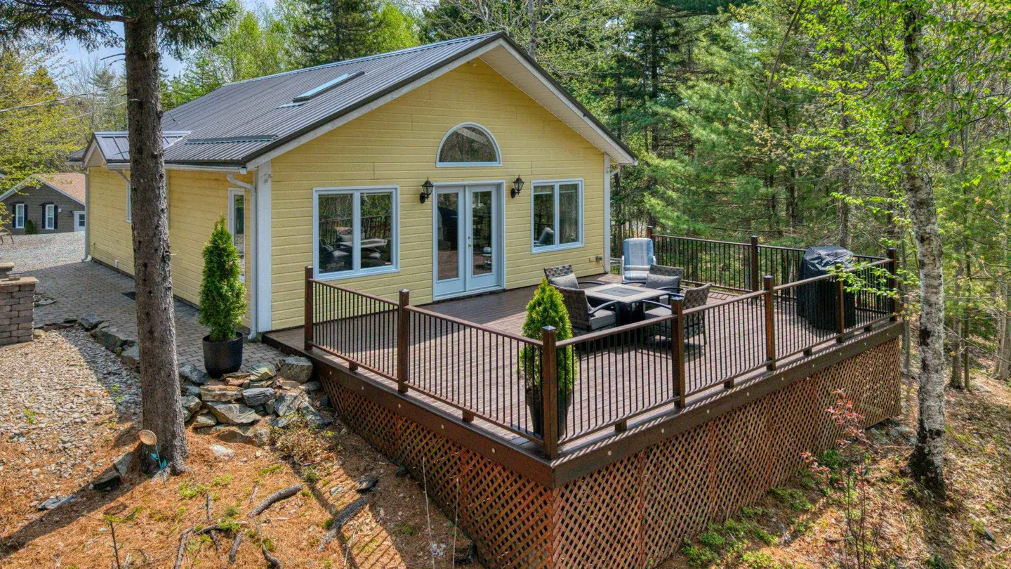Yellow house with a metal roof and a large deck with a table and chairs. The house is surrounded by trees.