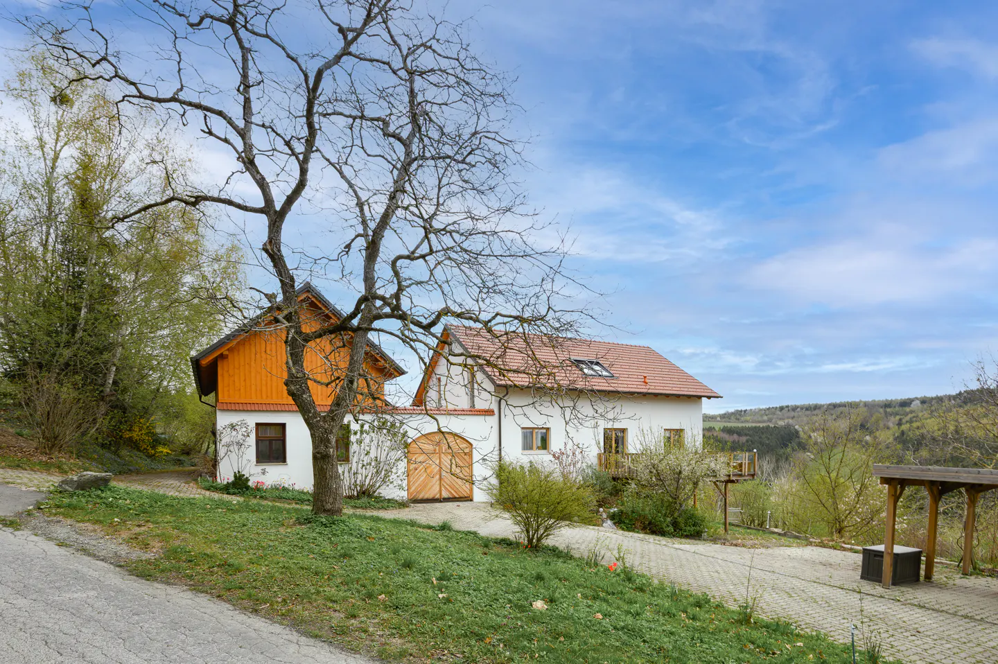 Exterior view of a white house with an orange roof, a bare tree in front, and a blue sky.