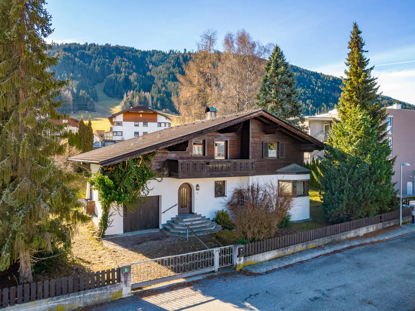 Two-story house with brown wood and white siding, a brown roof, and a small balcony. Mountains are in the background.