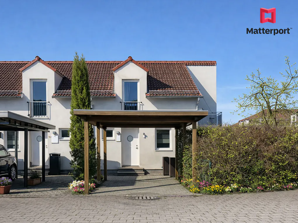 Exterior of a two-story white house with a brown tiled roof and a wooden carport. Flowers line the driveway.