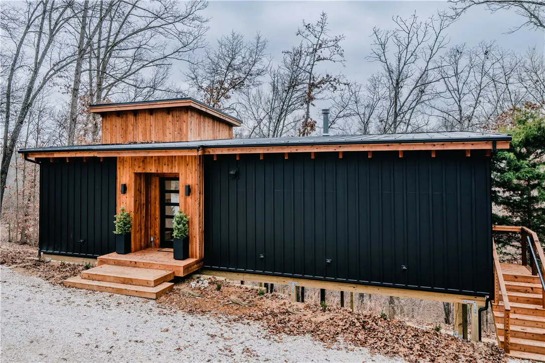 Modern black and wood cabin home with a flat roof, surrounded by trees.