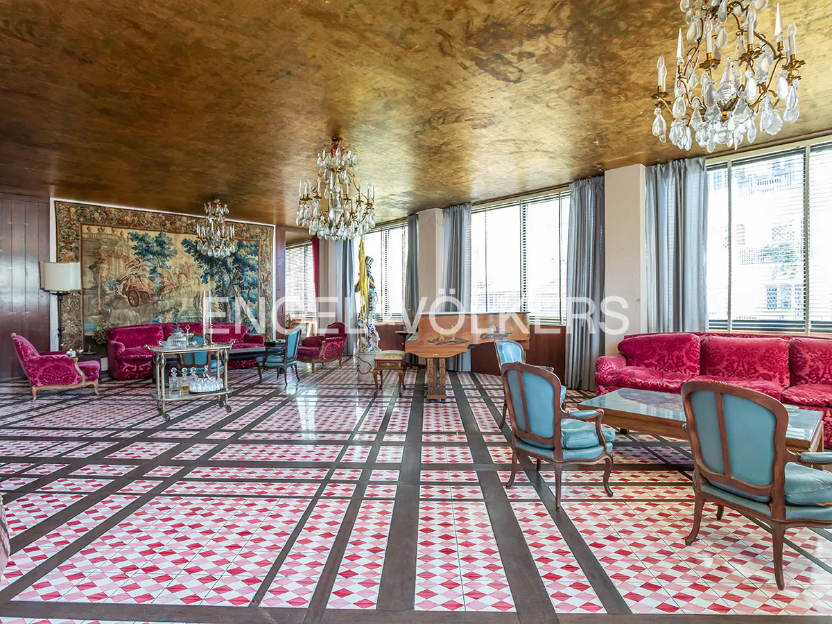 Luxurious living room with a gold ceiling, crystal chandeliers, red velvet sofas, blue armchairs, and patterned tile floors.