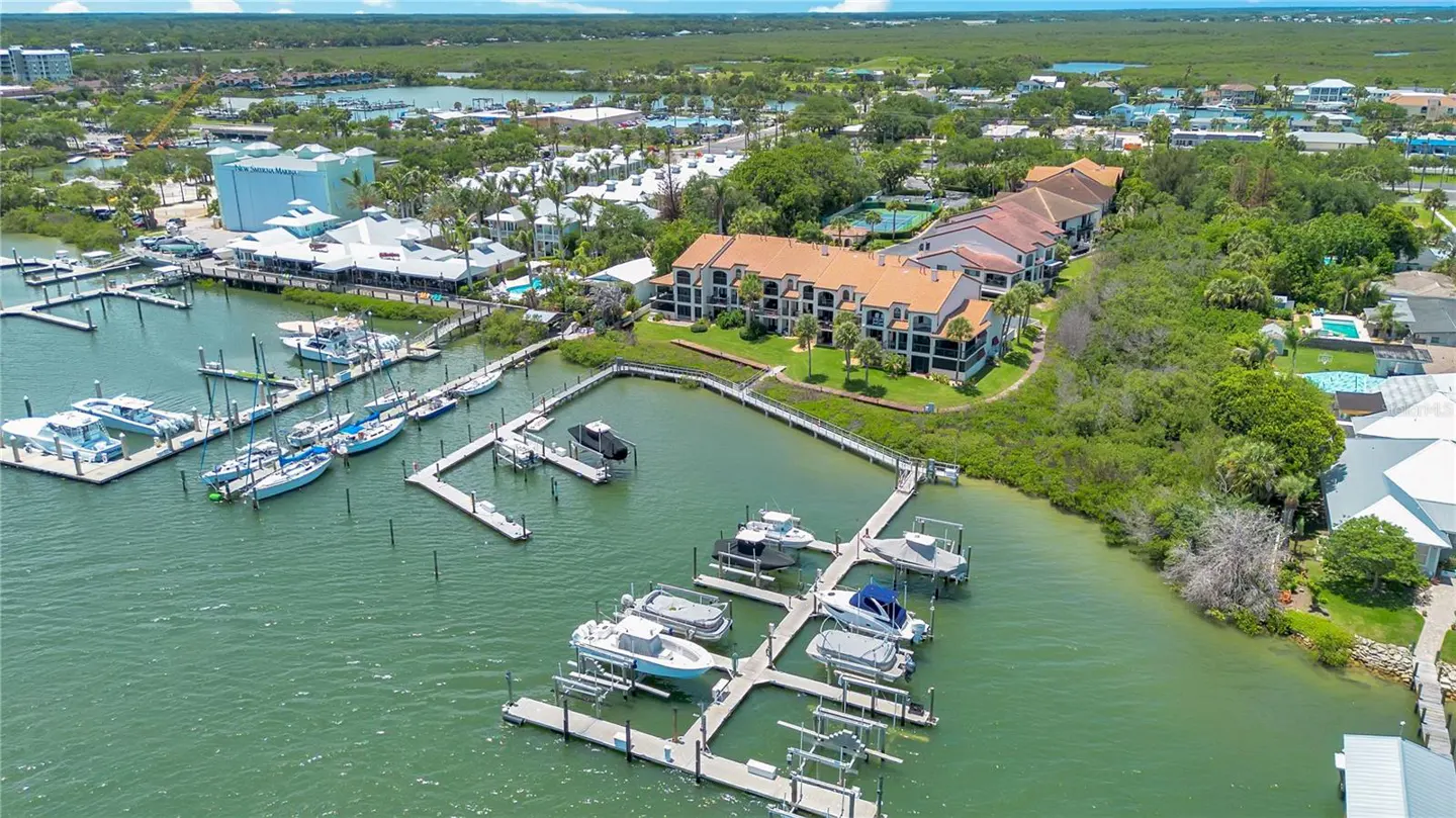 Aerial view of a waterfront condo complex with orange roofs, adjacent boat docks, and numerous docked motorboats.