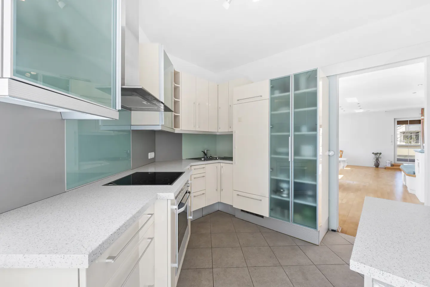 Bright kitchen with white cabinets, speckled countertops, and stainless steel appliances. A doorway leads to a living area with wood floors.