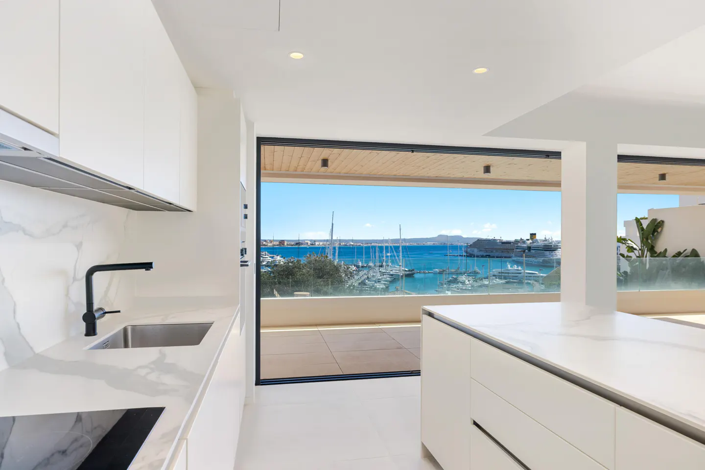 Bright, modern kitchen with white cabinets, marble countertops, and a black faucet. A large window offers a view of a marina with boats and blue water.