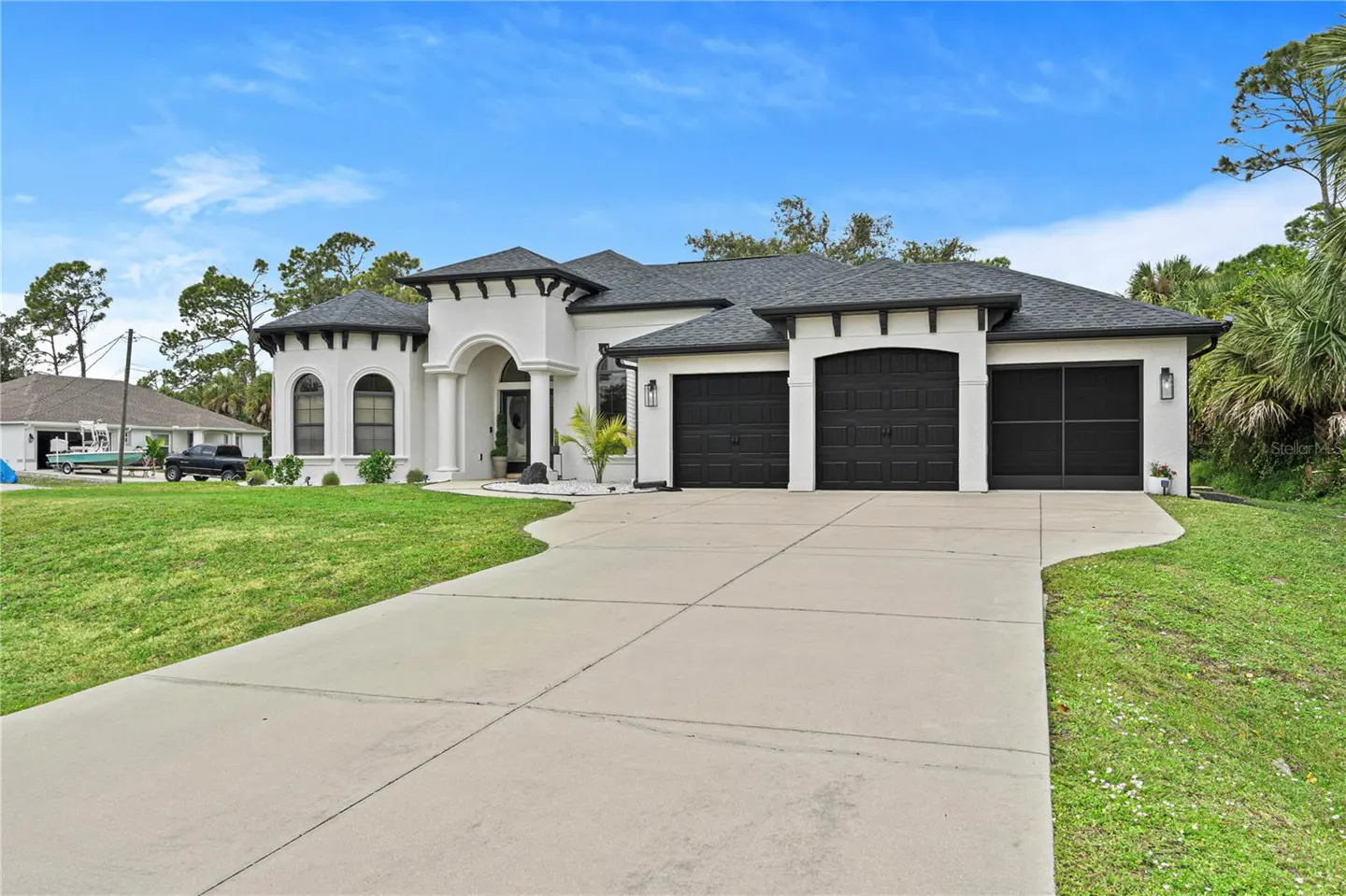 A white, single-story house with a three-car garage and a curved driveway. The house has black trim and a gray roof.