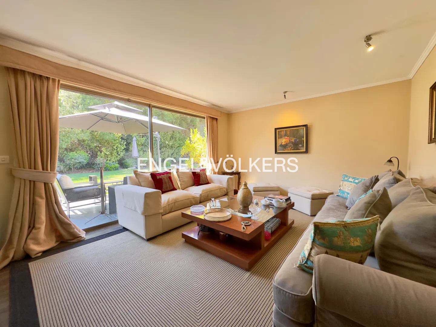 Living room with beige walls, sofas, and a large window overlooking a patio with an umbrella.