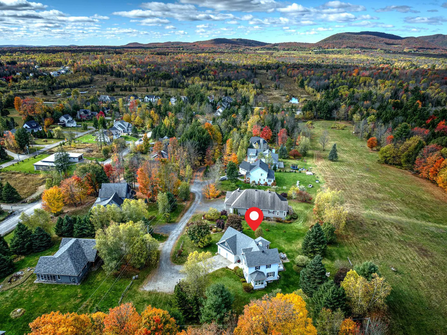 Aerial view of a white house with a red pin on the roof, surrounded by colorful autumn trees and other houses.