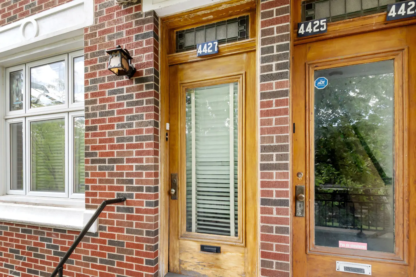 Two wooden front doors with glass panels and house numbers 4427 and 4425 set in a red brick building facade.