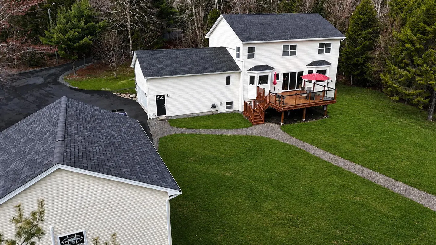 Aerial view of a white two-story house with a dark roof, a wooden deck with a red umbrella, and a green lawn.