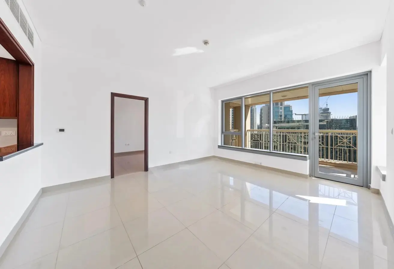 Empty room with white walls, glossy tile floors, a doorway, and a large window leading to a balcony with city views.