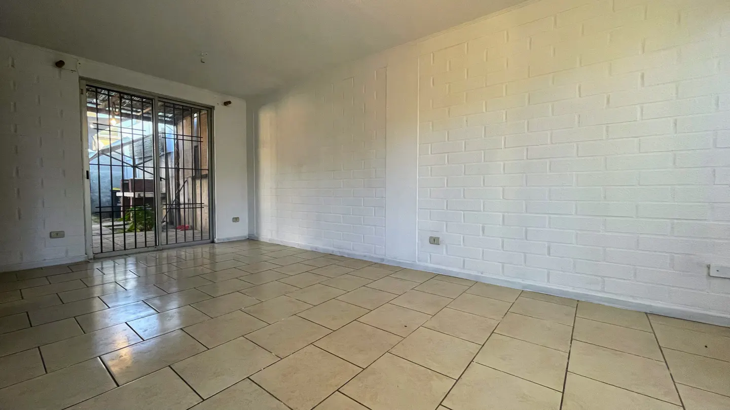 Empty room with white brick walls, beige tile floor, and sliding glass doors with black bars leading to a patio.