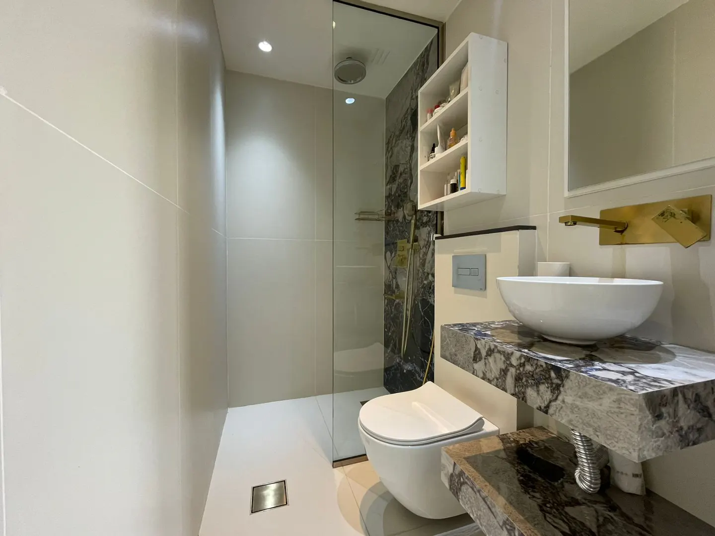 Modern bathroom with a glass-enclosed shower, white toilet, and marble countertop with a white vessel sink and gold faucet.