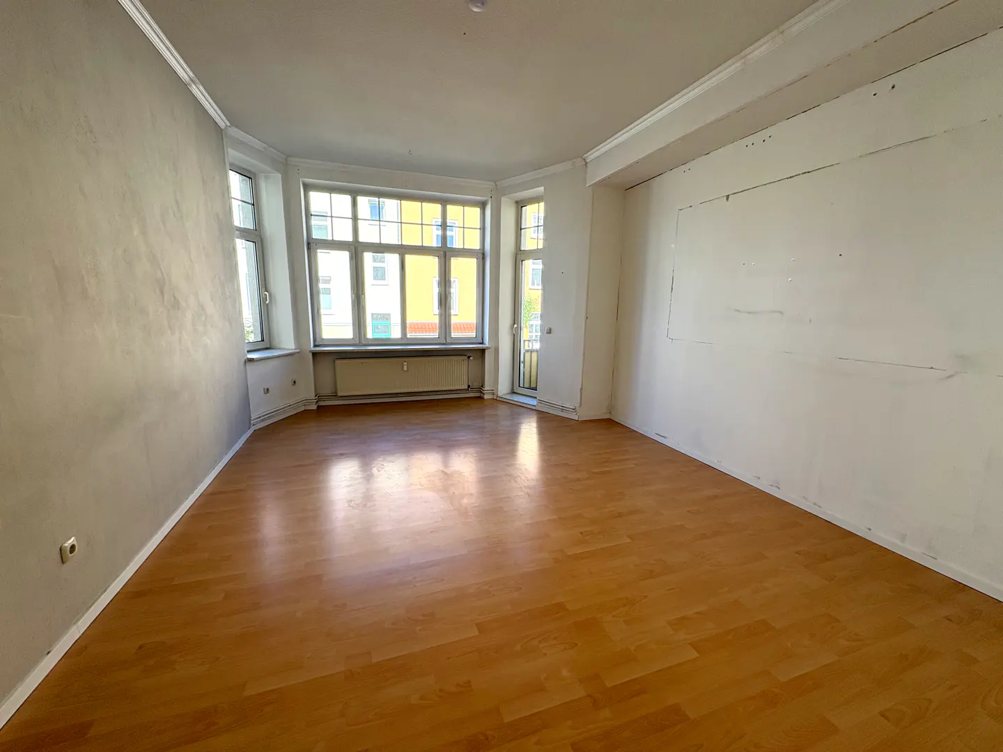 Empty room with light brown wood floors, white walls, and large windows. A radiator sits beneath the windows.