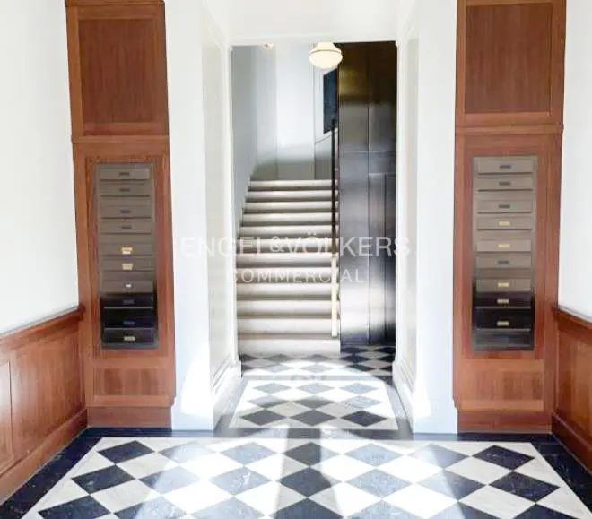 Hallway with black and white checkered floor, mailboxes in wood cabinets, stairs and elevator in the background.