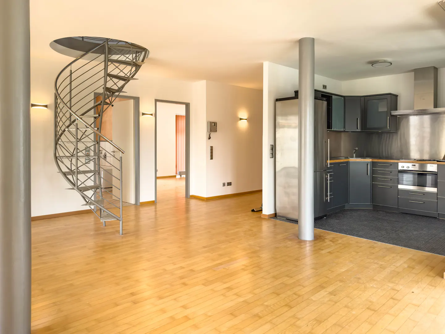 Open-concept apartment with a spiral staircase, hardwood floors, and a modern gray kitchen.
