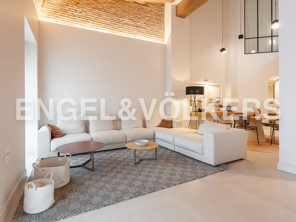 Modern living room with a large white sectional sofa, patterned rug, two coffee tables, and an exposed brick accent wall.