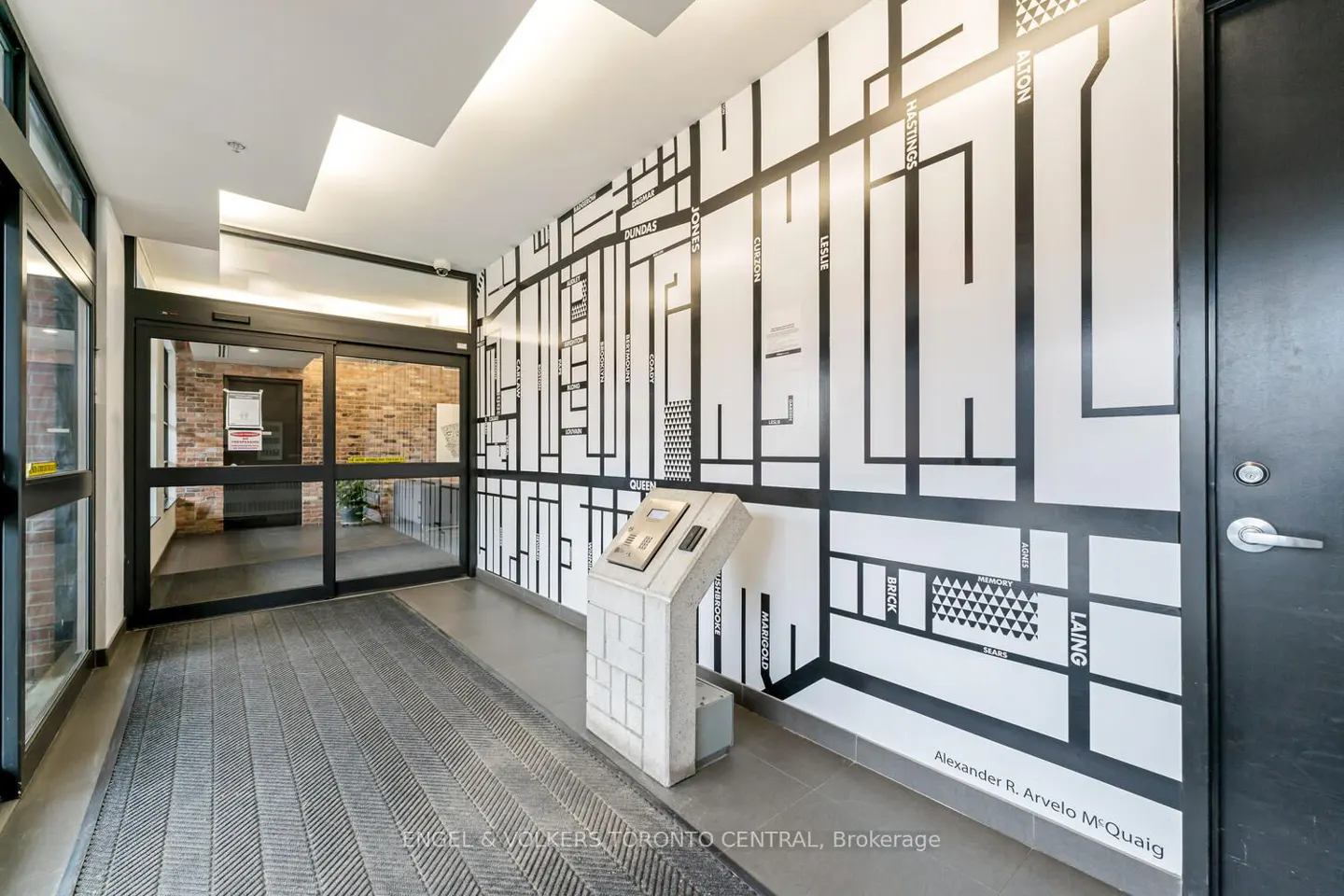 Condo lobby with automatic doors, gray mat, and a white wall map with black street names. A gray kiosk stands near the wall.