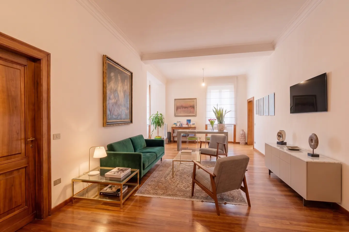 Living room with a green velvet sofa, two grey armchairs, a glass coffee table, and a modern sideboard on wood floors.