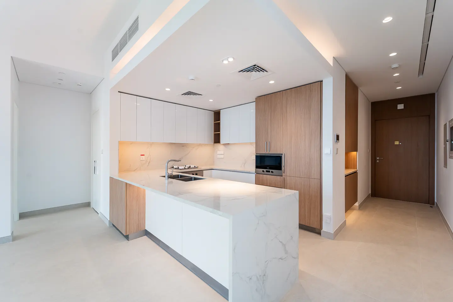A modern kitchen with white cabinets, a marble island, and wood accents. The room is brightly lit with recessed lighting.