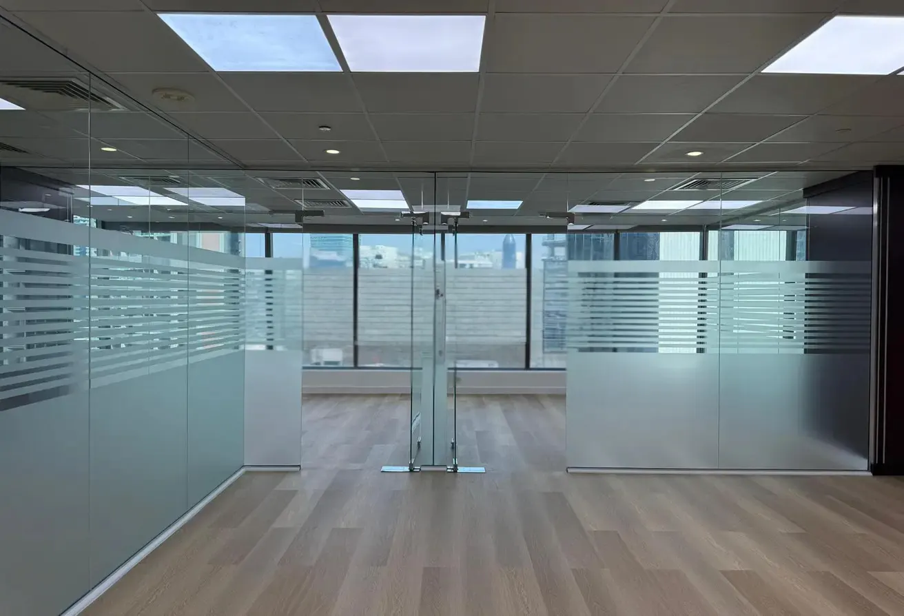 Empty office space with glass walls, horizontal frosted stripes, and wood floors. Cityscape visible through windows.