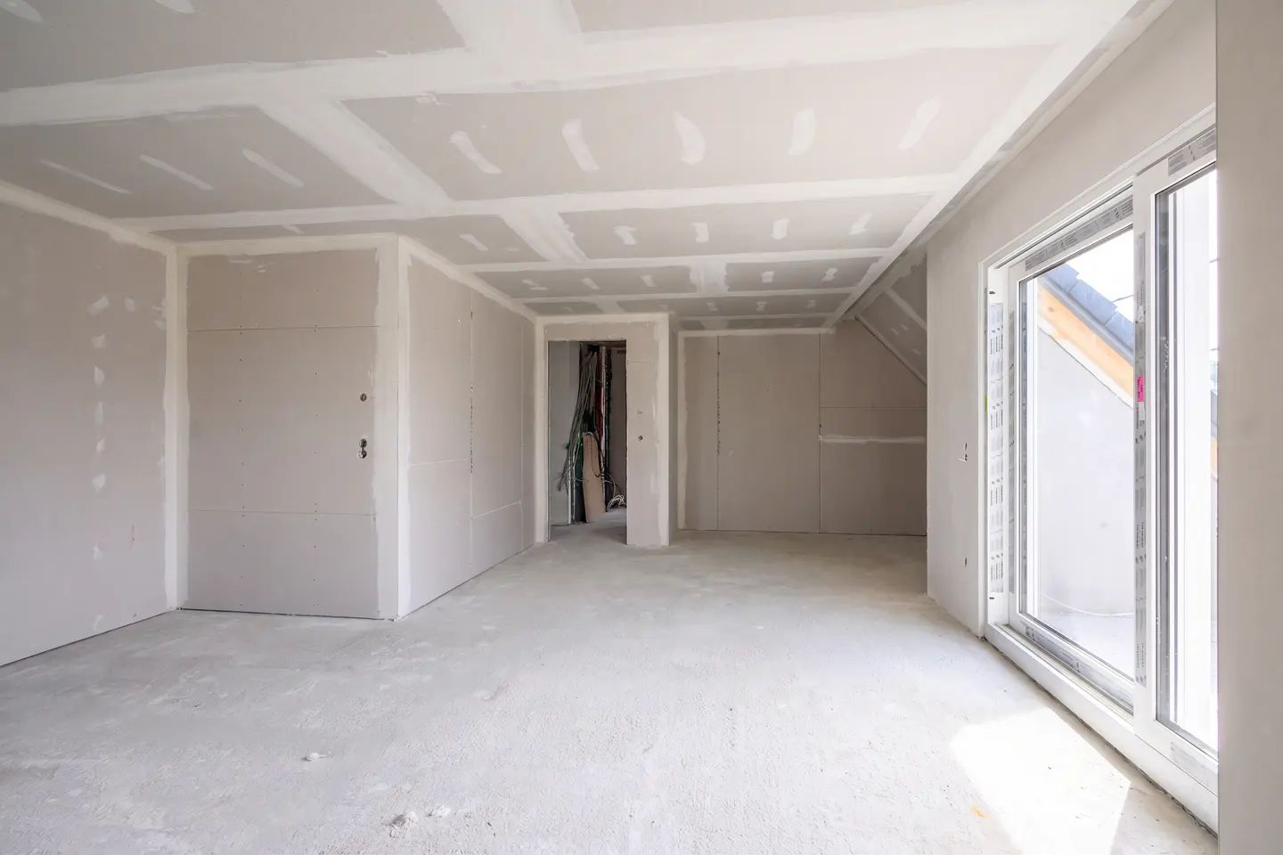 Unfinished room with drywall walls and ceiling, concrete floor, and sliding glass door.