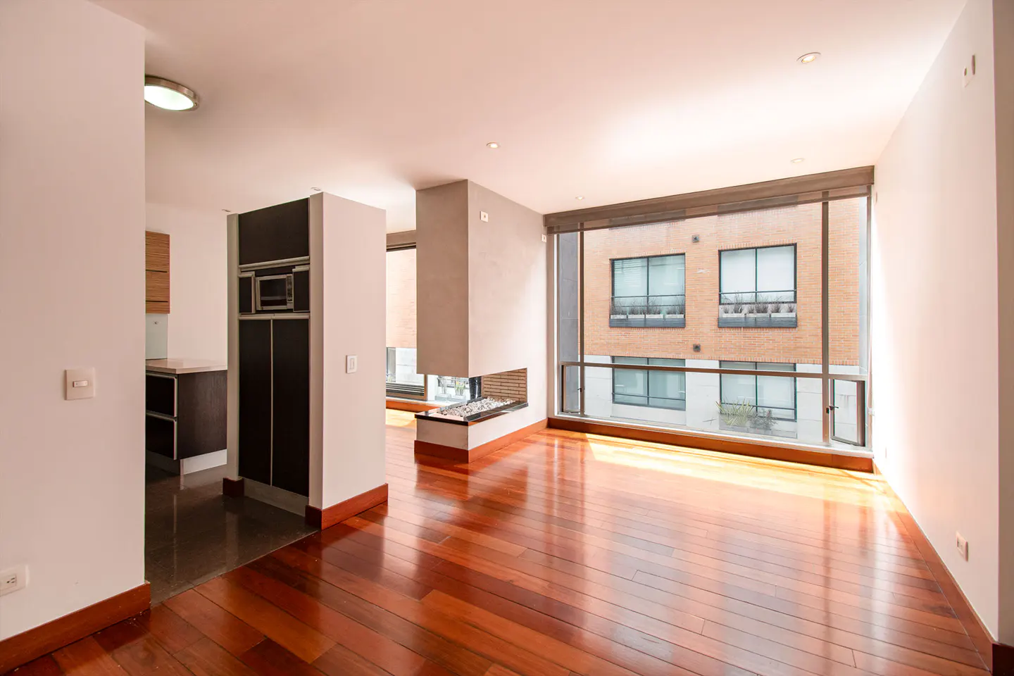 Bright, modern living room with hardwood floors, a fireplace, and a large window with a view of a brick building.