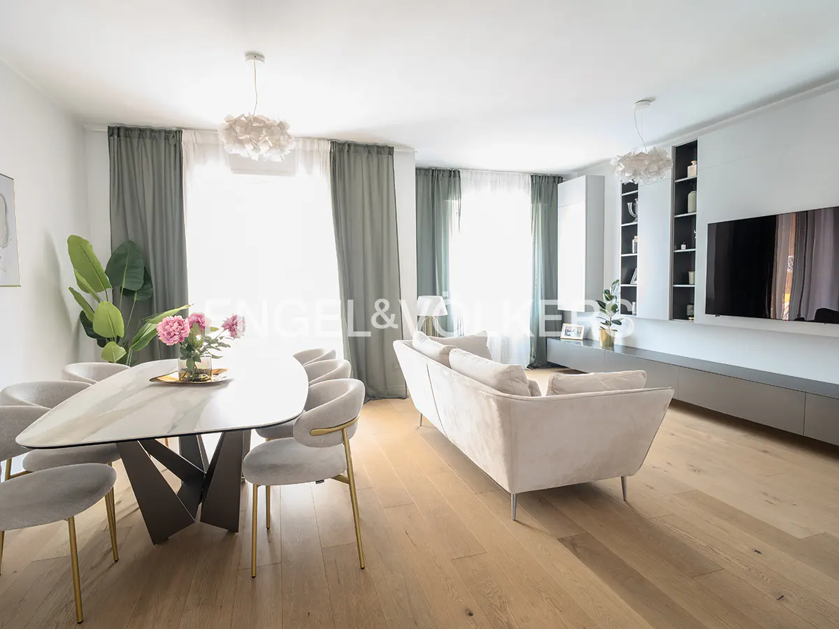 Open-concept living and dining area with a marble table, gray chairs, and a beige sofa on a light wood floor.