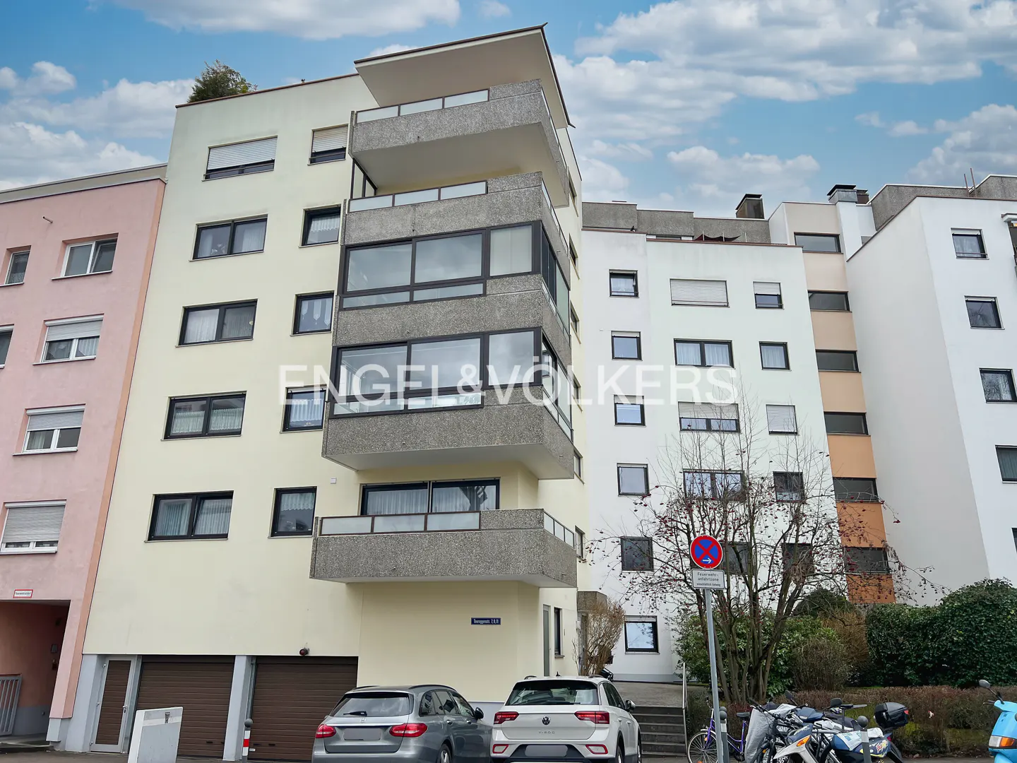 Exterior view of a multi-story apartment building with balconies, cars parked in front, and an Engel & Völkers logo.
