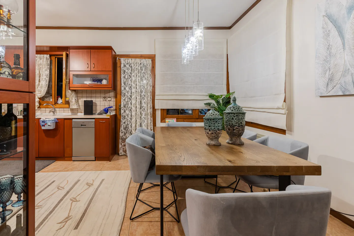 A dining area with a wooden table, grey chairs, and decorative vases. A kitchen area is visible in the background.
