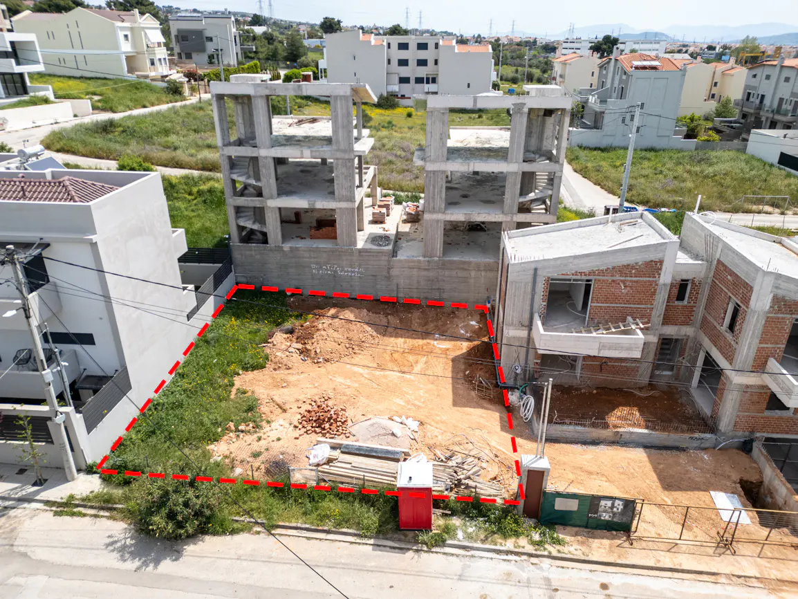 Aerial view of a vacant lot outlined in red, surrounded by buildings under construction in a residential area.