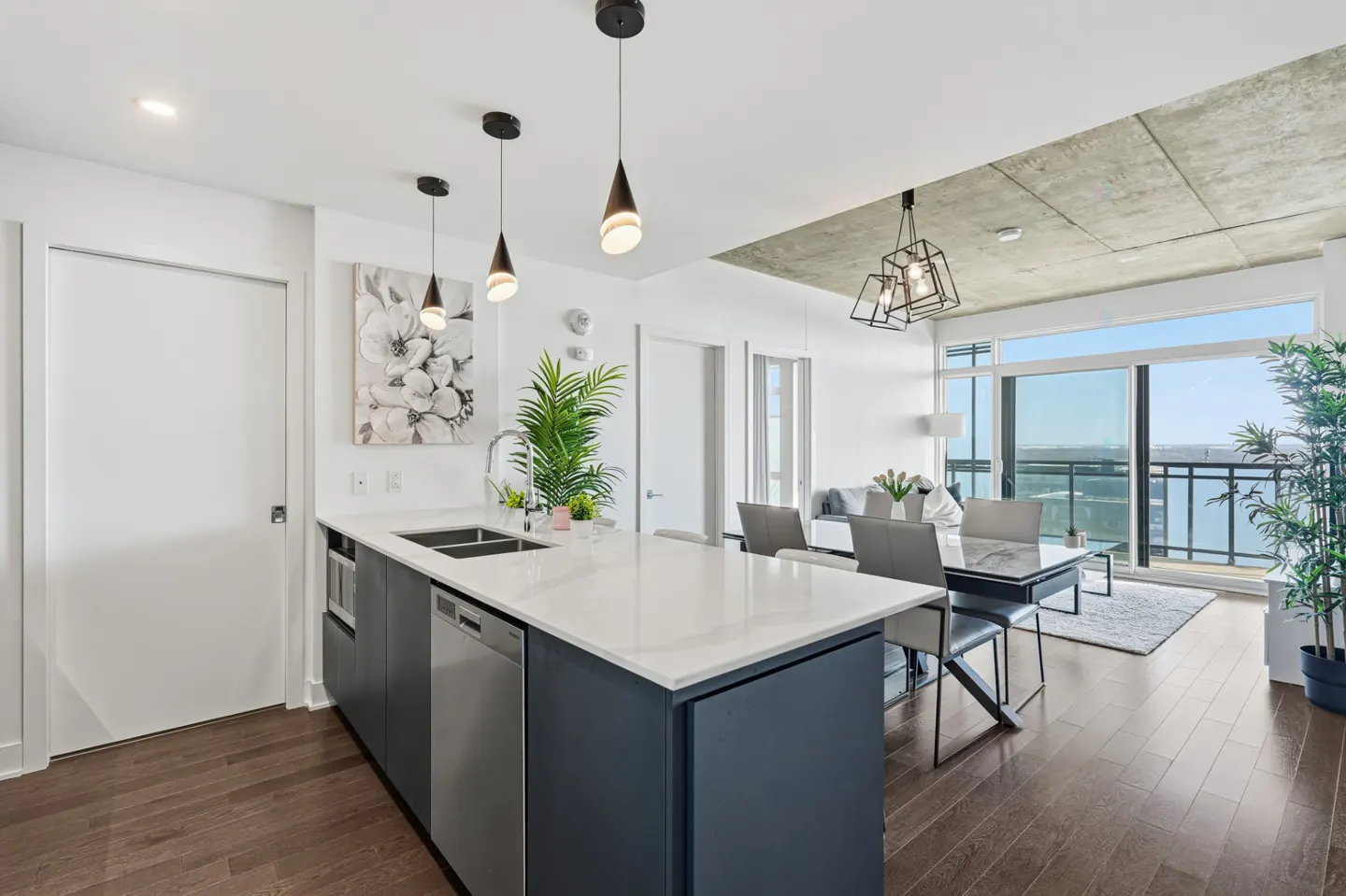 Modern kitchen with dark blue island, white countertops, and dining area with floor-to-ceiling windows and city views.