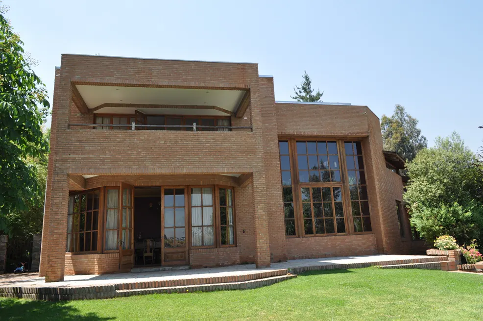 Two-story brick house with large windows and a balcony overlooking a green lawn.