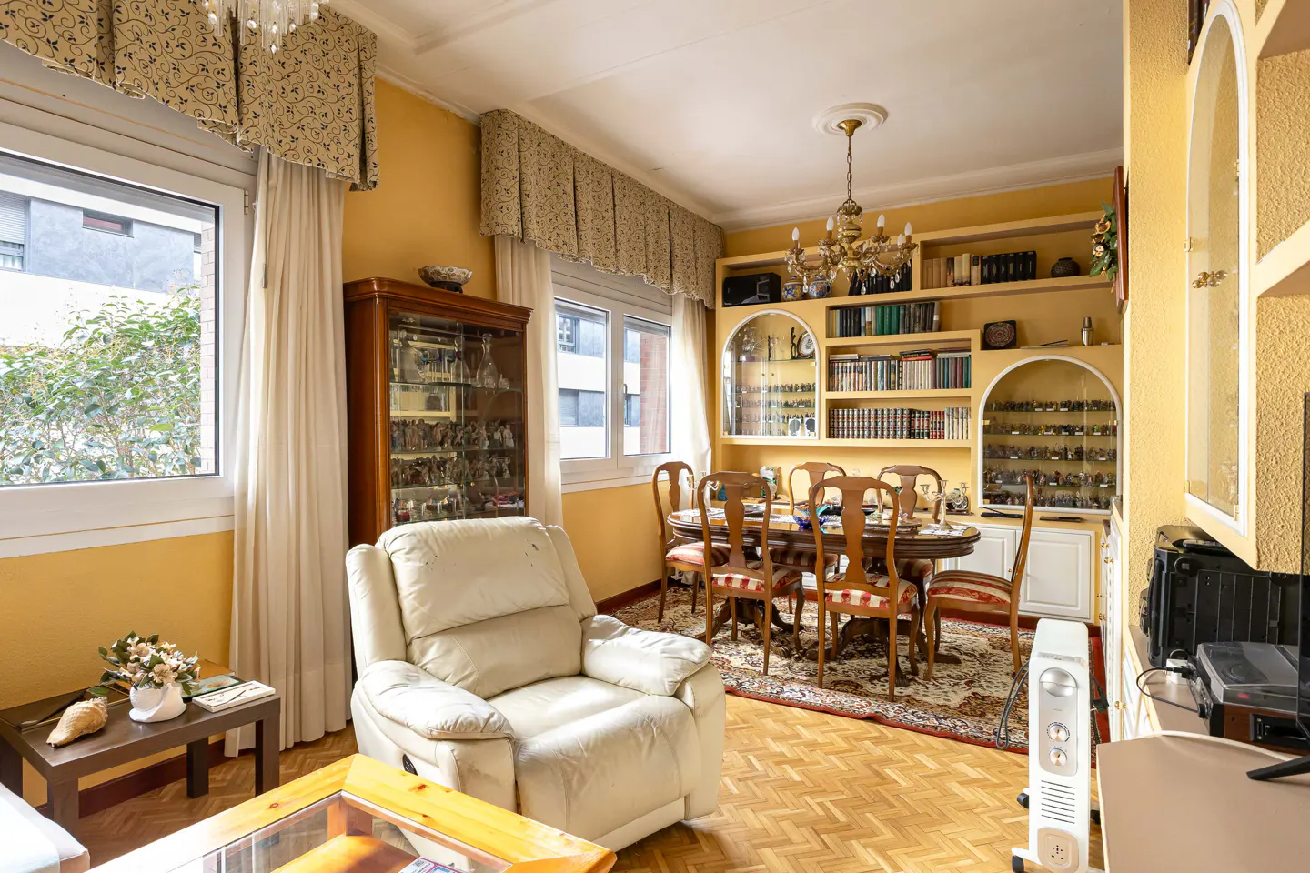 A living room with yellow walls, a dining table with chairs, a white recliner, and built-in bookshelves.