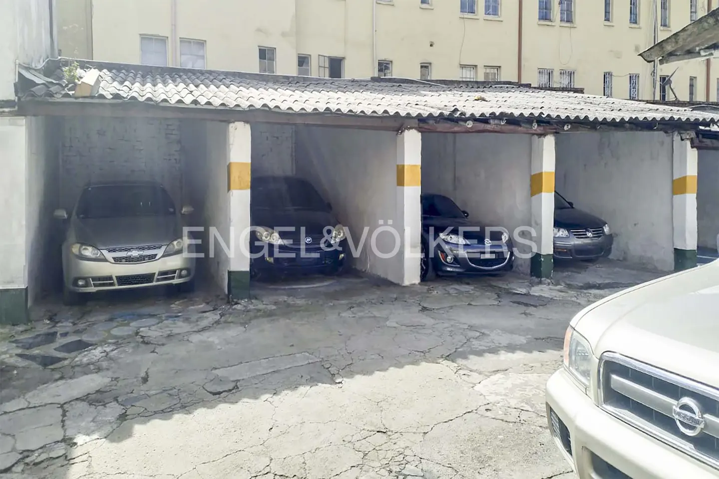Four cars parked in individual carport spaces with white columns and yellow stripes.