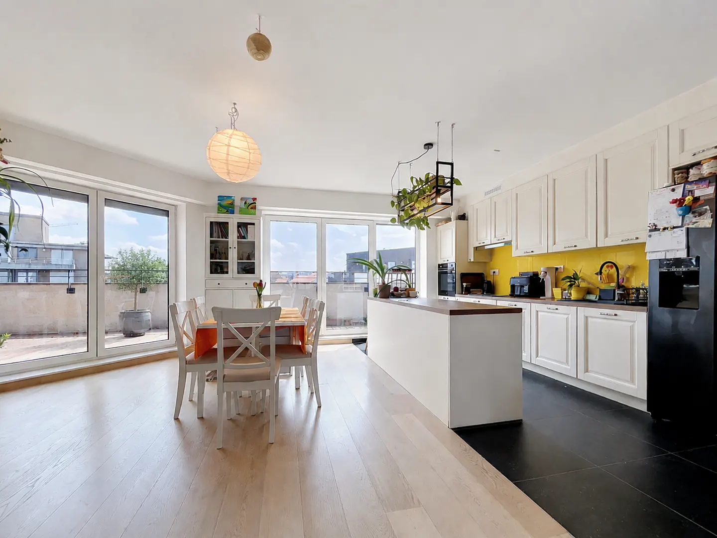 Bright, modern kitchen with white cabinets, yellow backsplash, and island. Dining table with orange accents near sliding glass doors to a balcony.