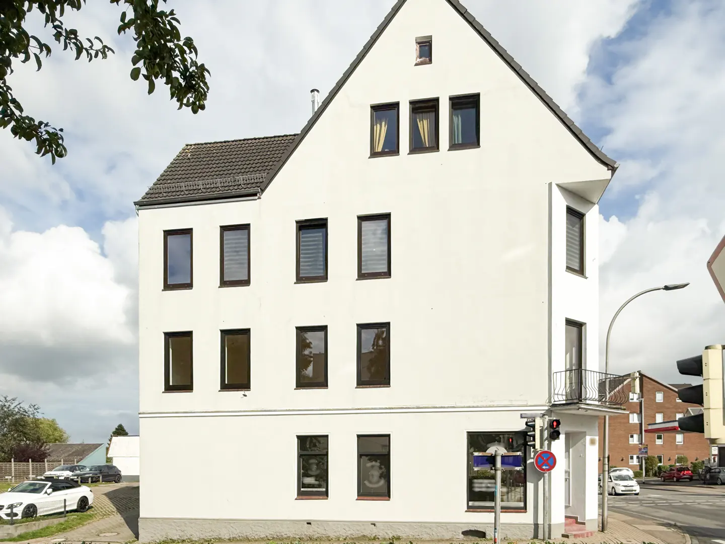 A three-story white building with a gray roof and dark-framed windows. A small balcony is on the second floor.