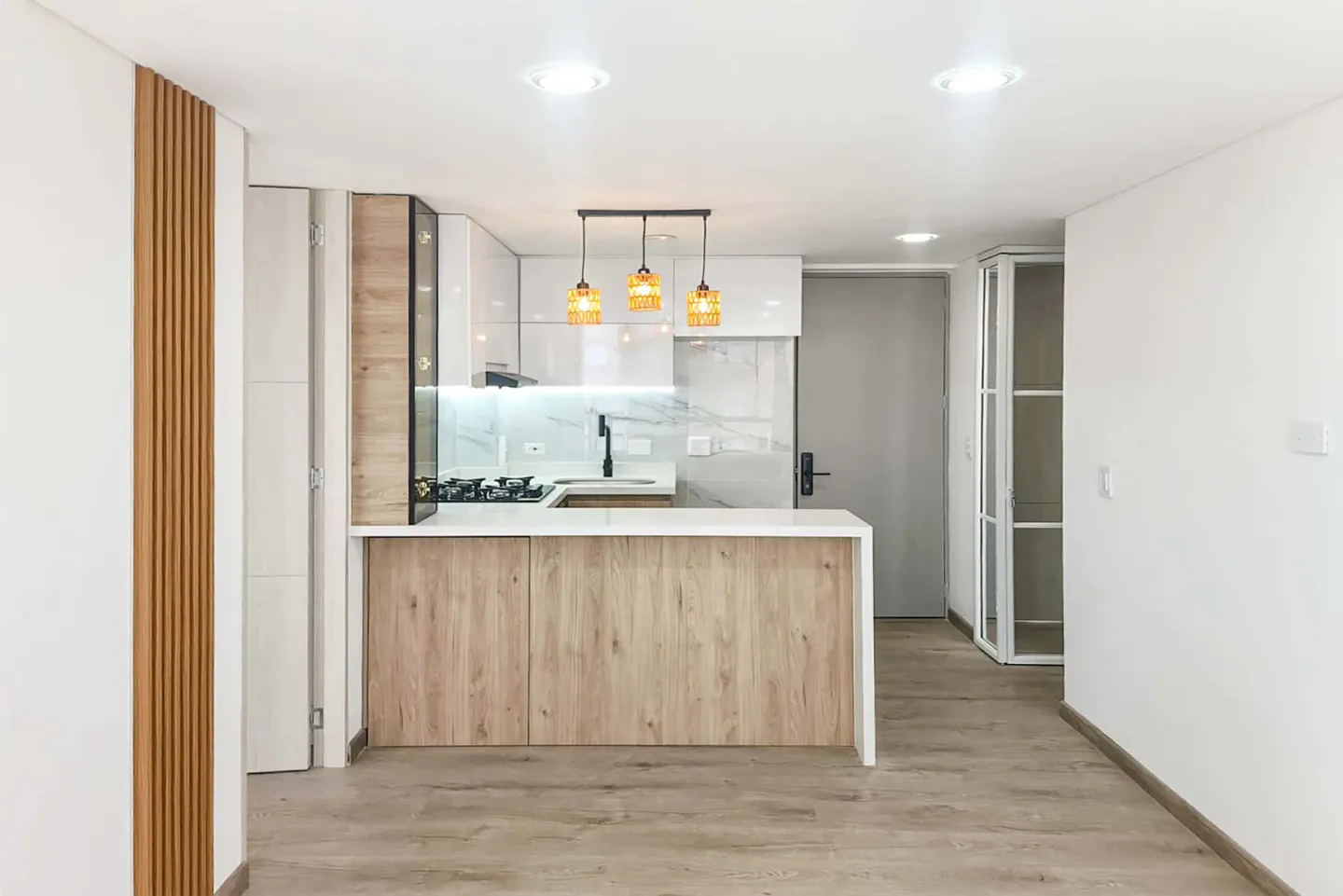 Bright, modern kitchen with white cabinets, wood-look island, and three orange pendant lights. Wood floors and white walls.